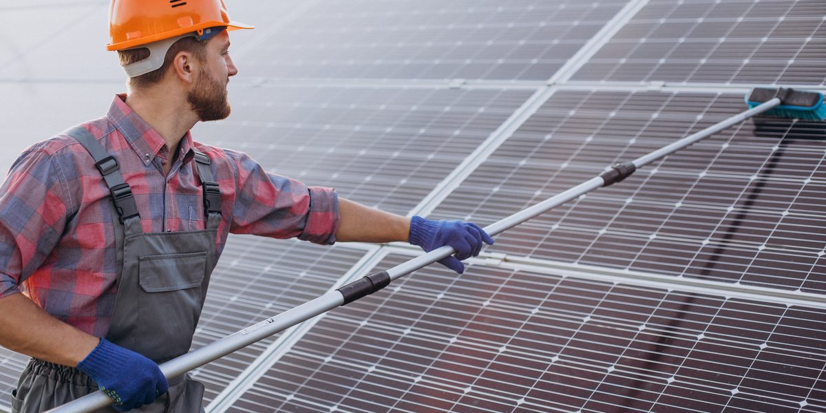 Worker cleaning solar panels with a long-handled soft brush