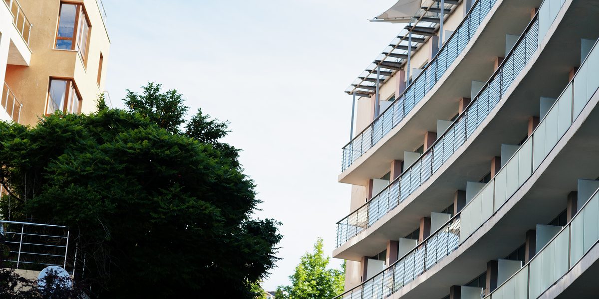 Curved condominium building with glass-railed balconies among trees