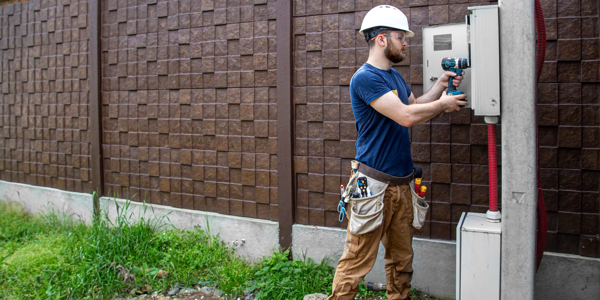 Electrician working at an outdoor electric meter and utility box on a house wall