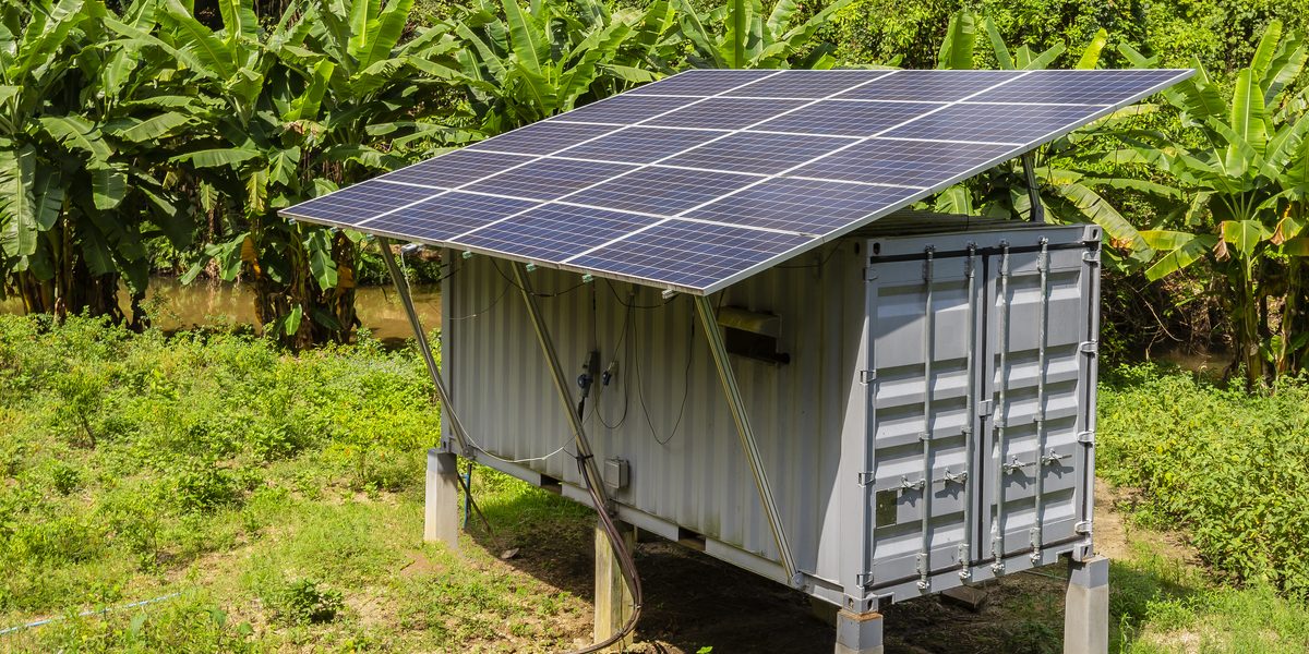 Solar panels mounted over a small shed-style building surrounded by greenery