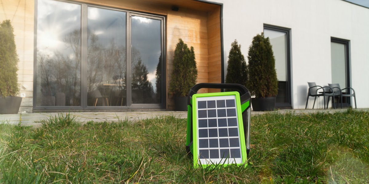 Small portable solar panel standing on the lawn in front of a house patio, illustrating a ground-placed panel in a yard