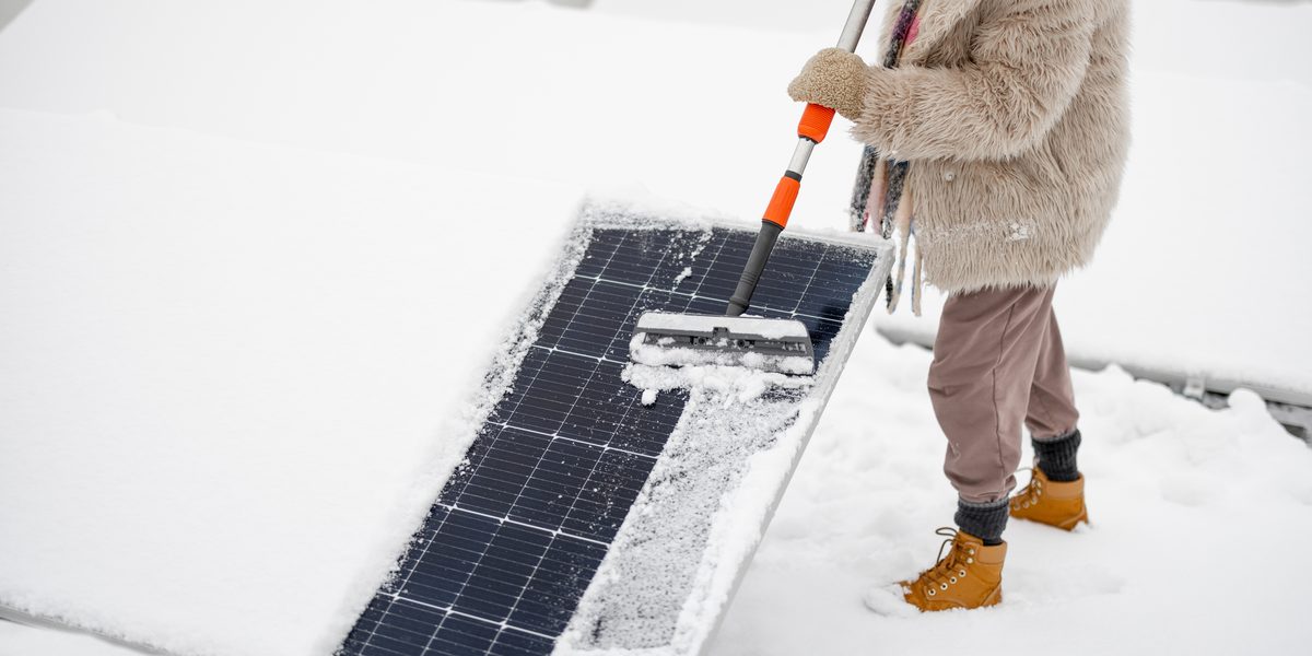Person brushing snow off a solar panel with a long-handled brush